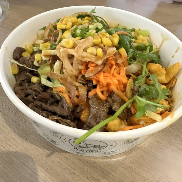 Vietnamese beef bowl with corn, carrots, fried onions, and cilantro in a white bowl.