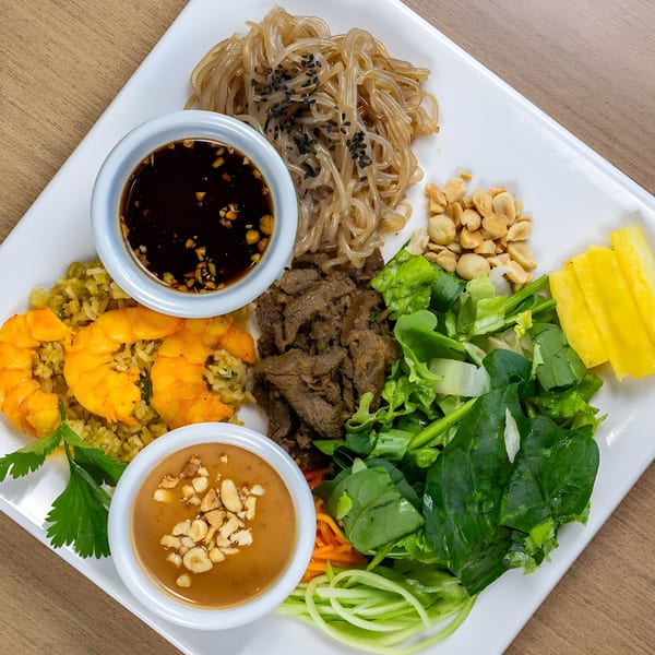 A Vietnamese platter with glass noodles, beef, shrimp fried rice, salad, peanuts, mango, and two dipping sauces.