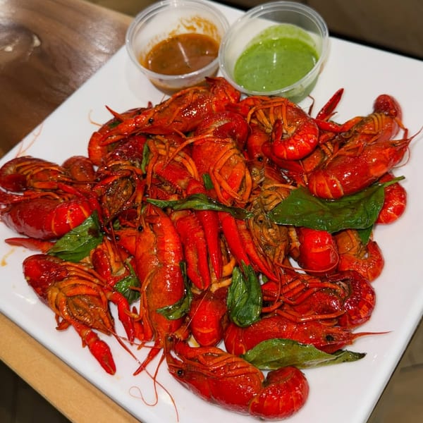 A white plate piled high with bright red crawfish, green herbs, and two dipping sauces.