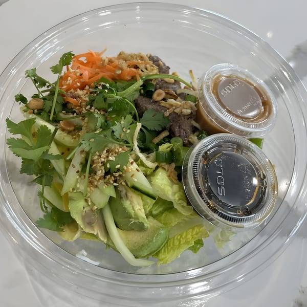 Vietnamese beef salad with avocado, cilantro, carrots, and two sauces in a clear to-go container.