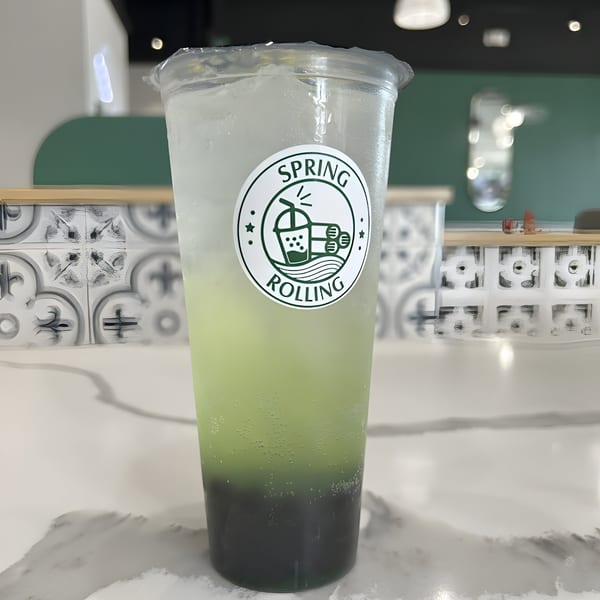 A Spring Rolling branded drink with dark green liquid at the bottom, light green in the middle, and clear on top.
