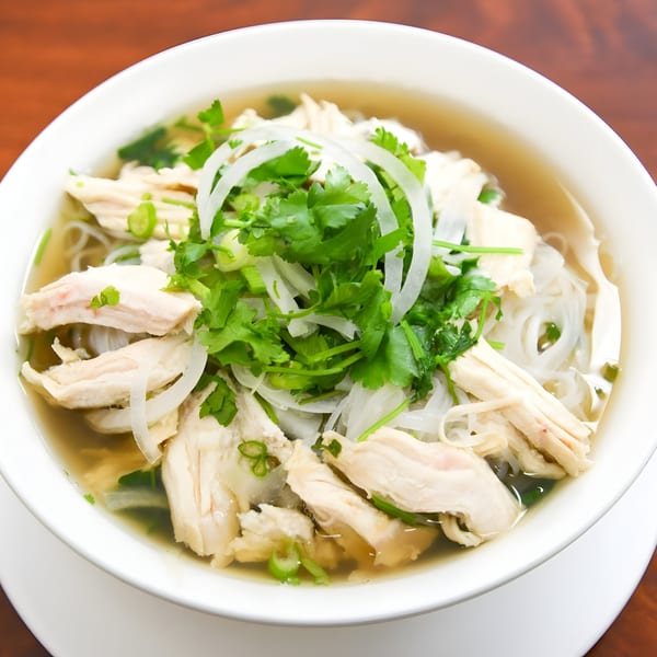 A bowl of Vietnamese chicken pho with rice noodles, sliced onions, and fresh cilantro.