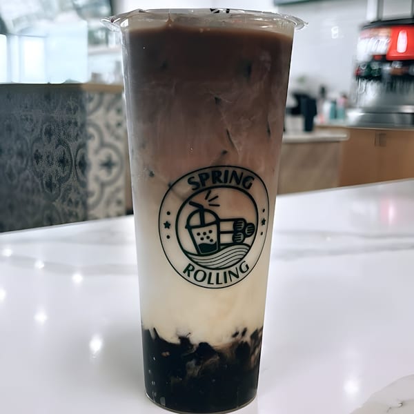 A Spring Rolling branded bubble tea with dark brown and white layers, on a white counter.